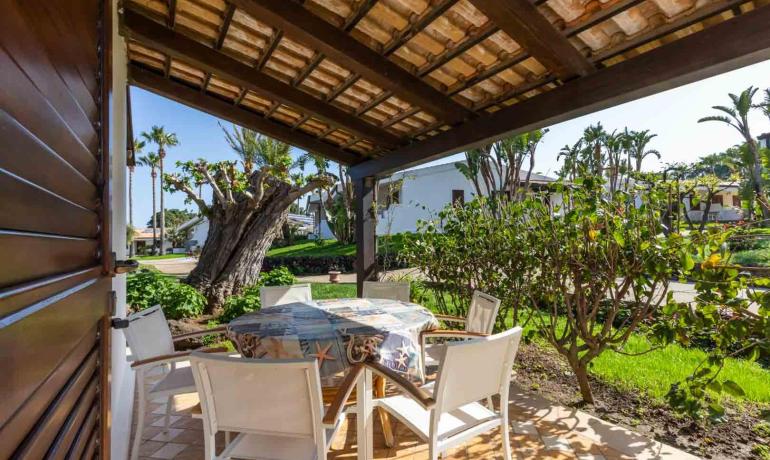 Terrazza accogliente con tavolo e sedie, circondata da verde rigoglioso e sole.