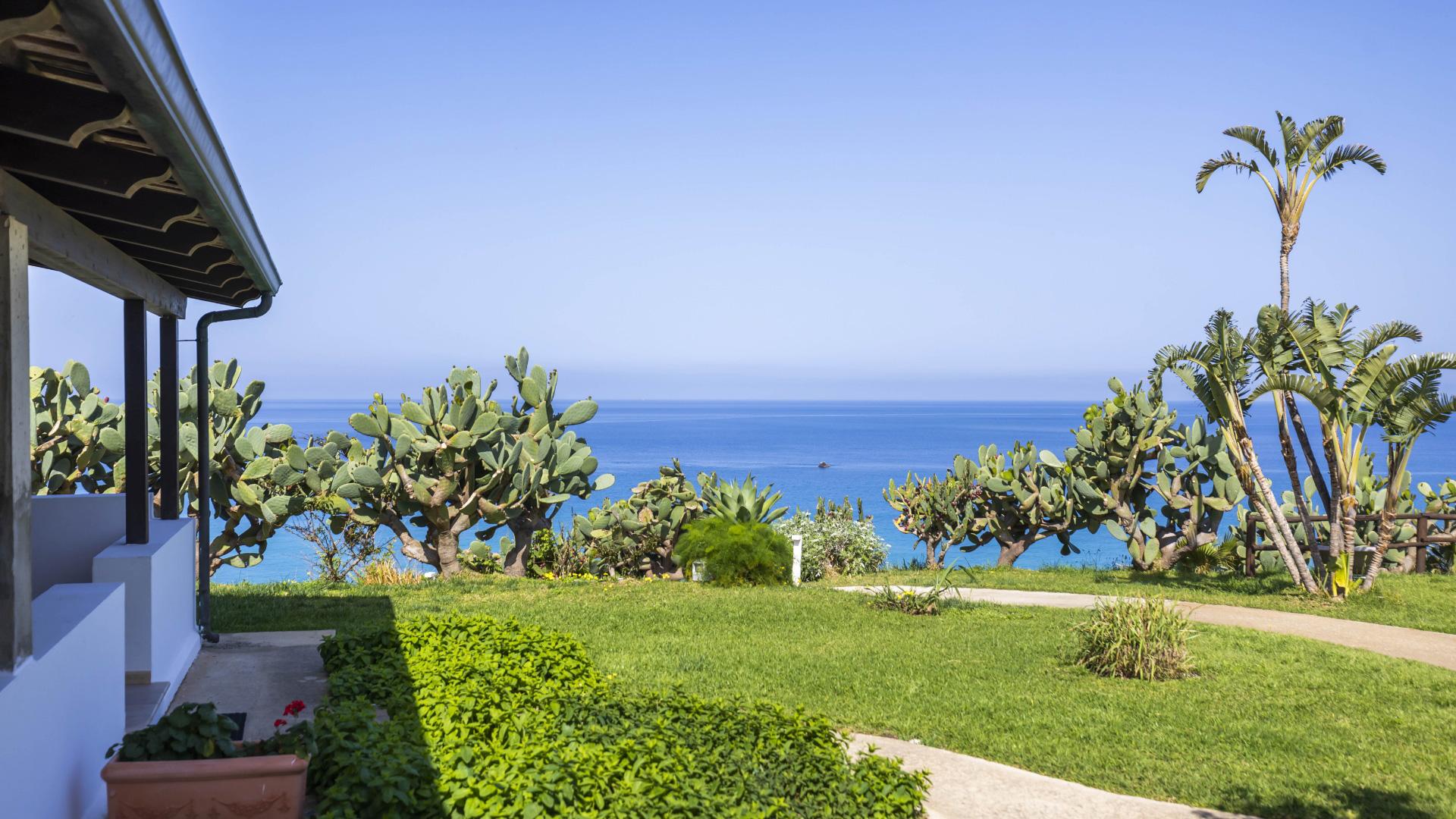 Vista sul mare con giardino, cactus e palme.