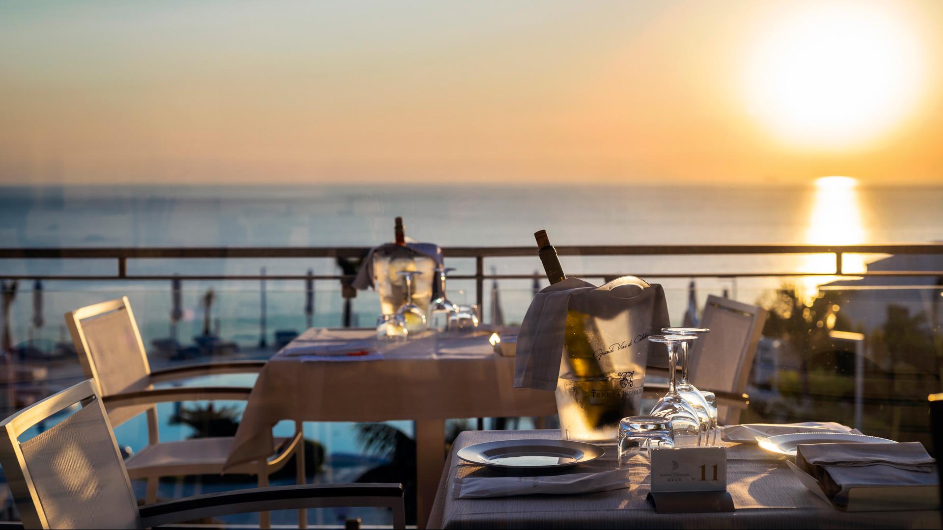 Romantisches Abendessen bei Sonnenuntergang mit Meerblick, Wein und Gläsern.