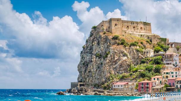 Burg auf einer Klippe mit bunten Häusern und Strand am Meer.