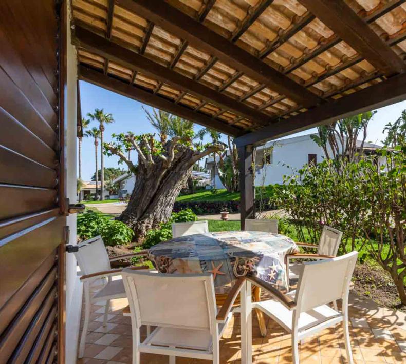 Veranda with table and chairs, green garden and trees.