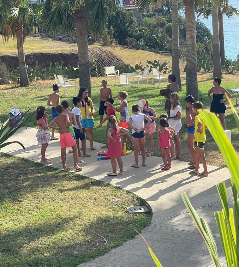 Children playing outdoors under palm trees near the sea.