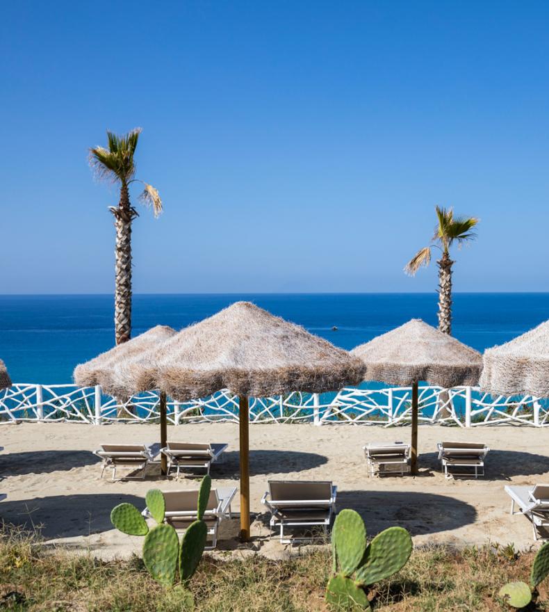 Spiaggia con ombrelloni di paglia, lettini e vista mare.