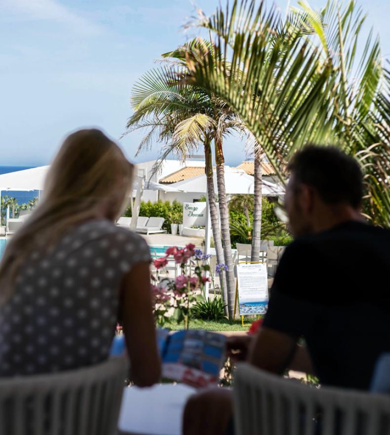 Due persone rilassate in un resort con piscina e vista mare.